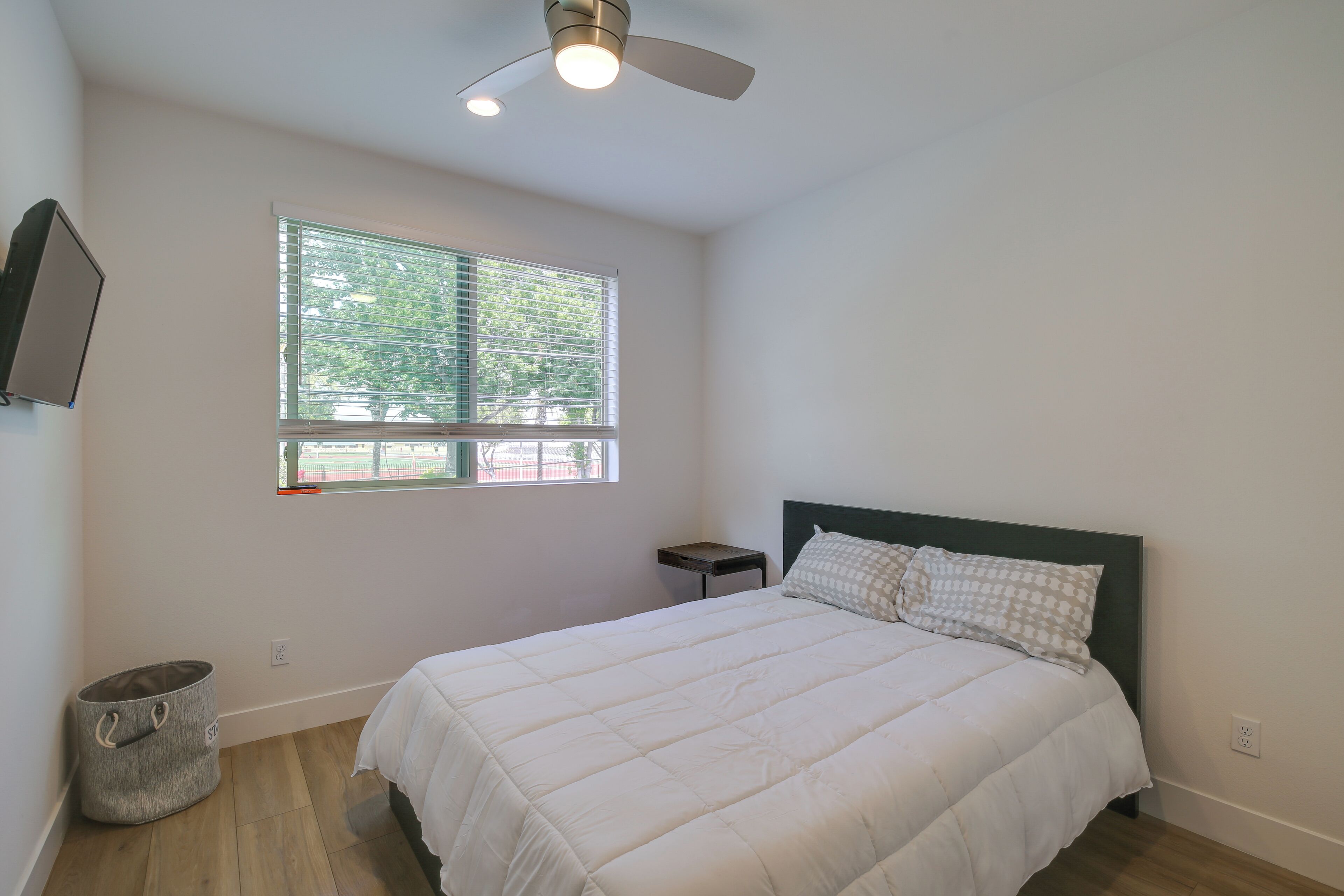 A bedroom with a bed, a window, a ceiling fan, and a small table.