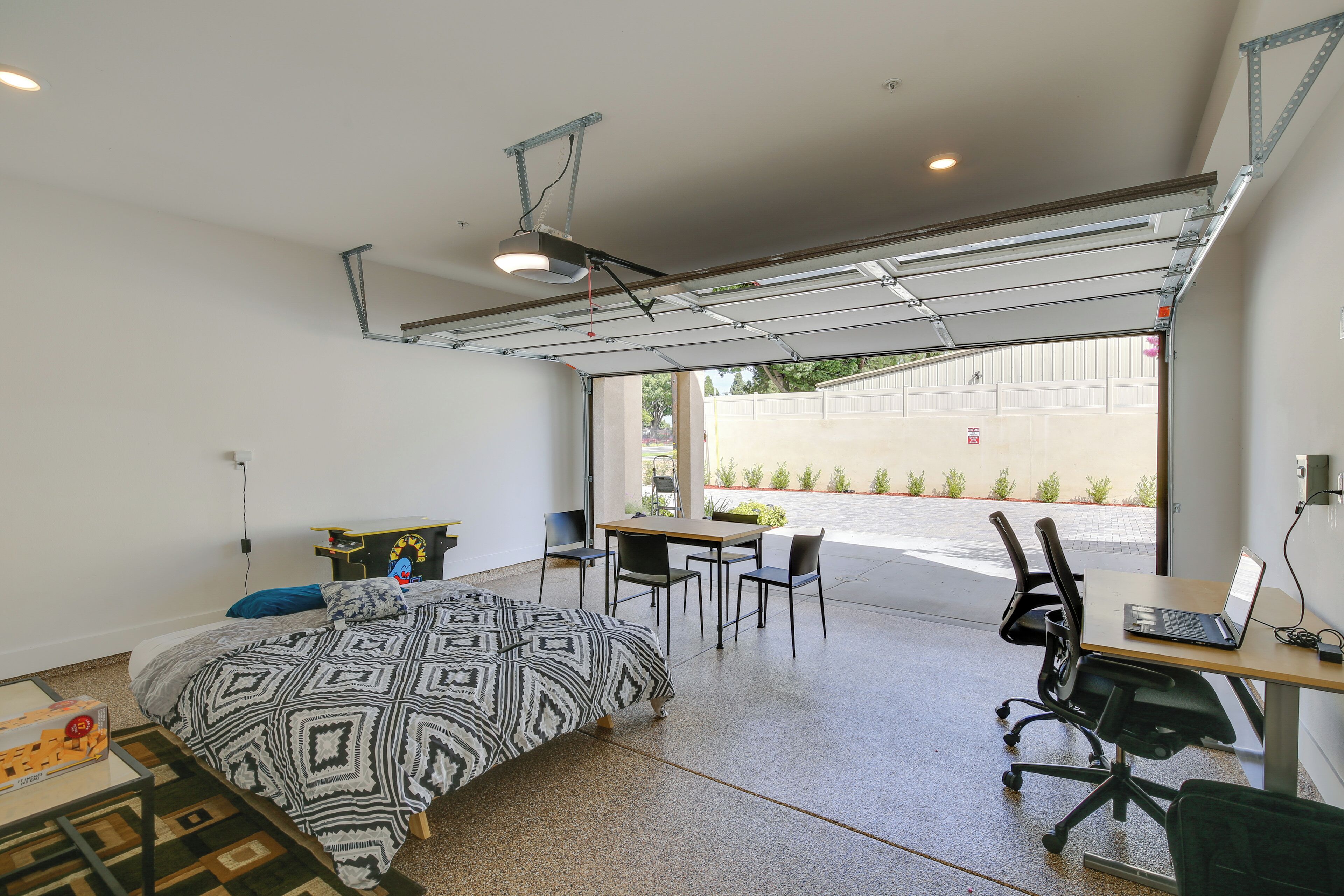 Une chambre moderne avec un lit, un bureau et des chaises, une porte de garage et une vue sur l’extérieur.