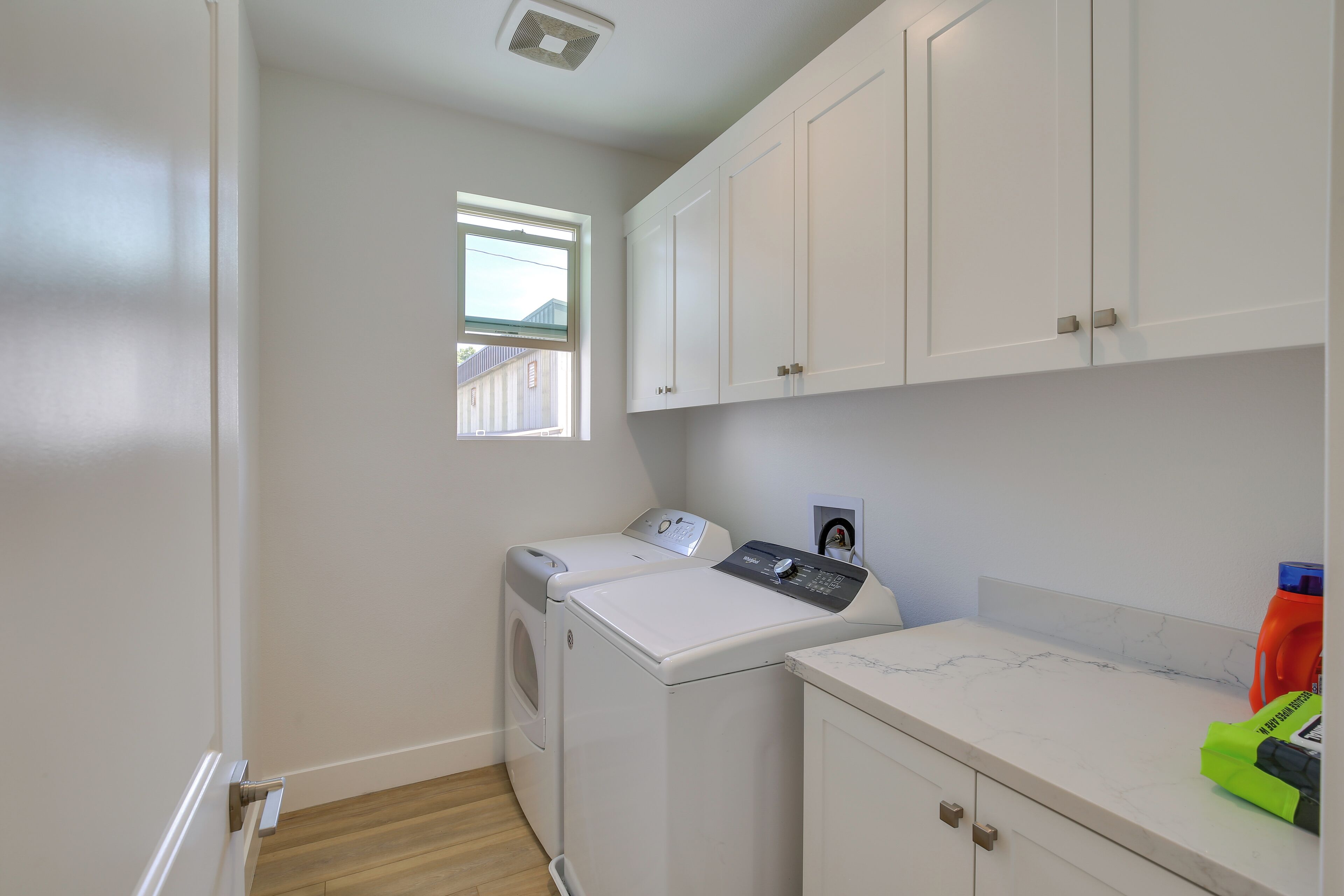 A laundry room with a washing machine and dryer, a window, and a countertop with a bottle of detergent.