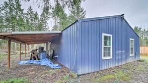 A blue metal shed with a wooden roof, a concrete block, and a hose on the ground. - Quaint, Cozy Outdoor Retreat Near Mt Rainier! (Roy)
