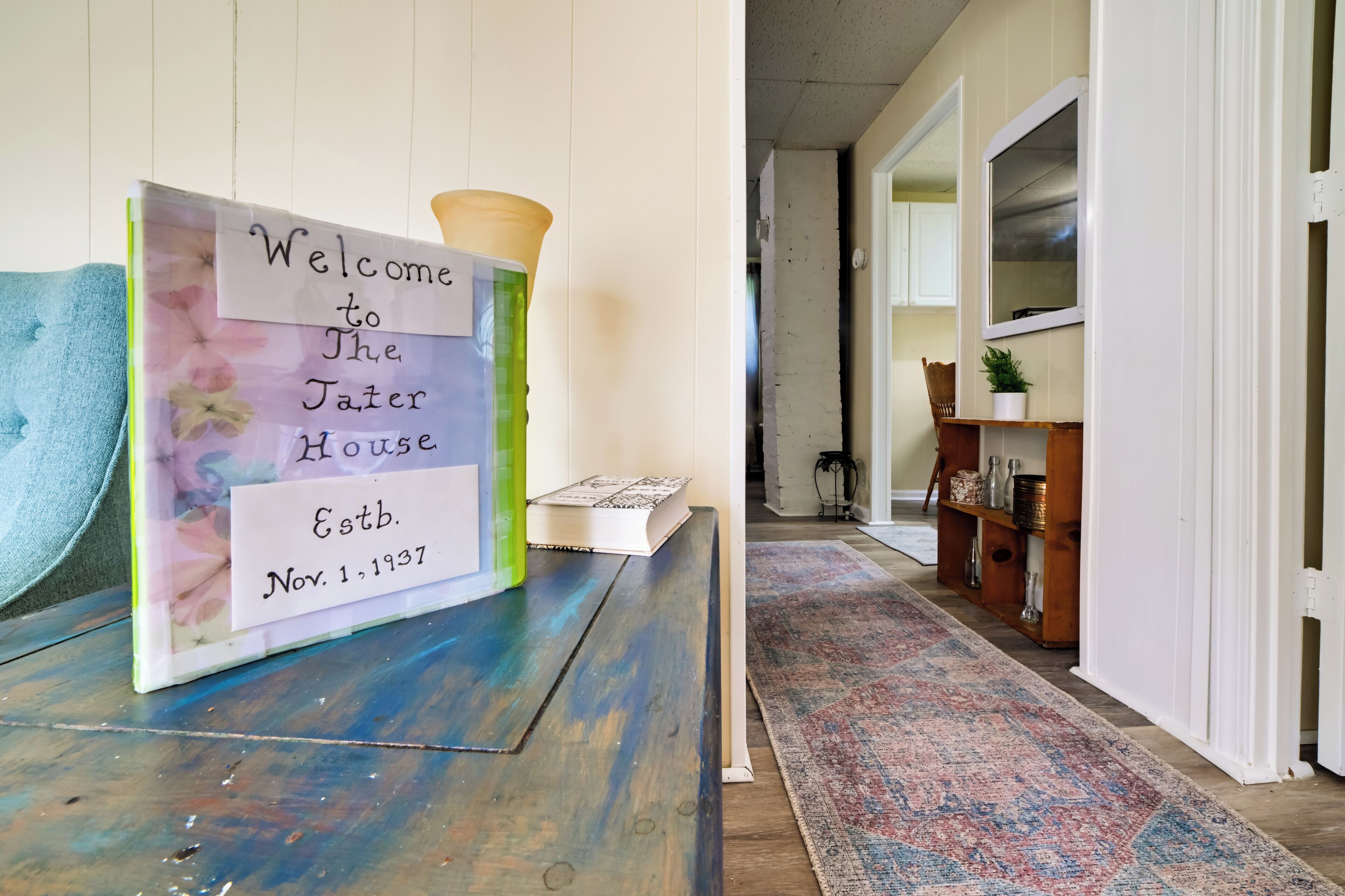 A welcome sign in a hallway with a patterned rug and wooden furniture.