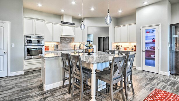 A modern kitchen with white cabinetry, a granite countertop, and a central island with chairs. There are built-in ovens and a refrigerator. - Modern Amarillo House w/ Fire Pit + Hot Tub! (Amarillo)