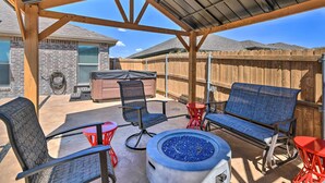 A covered patio area with a fire pit, outdoor furniture, and a brick house in the background. - Modern Amarillo House w/ Fire Pit + Hot Tub! (Amarillo)