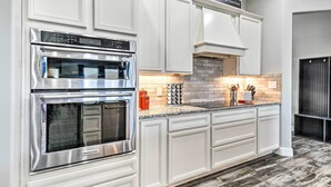 A modern kitchen with white cabinetry, stainless steel appliances, a granite countertop, and a brick backsplash. - Modern Amarillo House w/ Fire Pit + Hot Tub! (Amarillo)