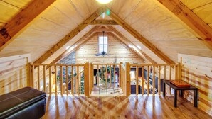 Un dormitorio estilo ático con techo inclinado, una ventana, un ventilador de techo y un banco de madera.