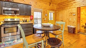 Interior de una cabaña de madera con cocina equipada con electrodomésticos de acero inoxidable, una mesa de comedor con sillas y una ventana pequeña.