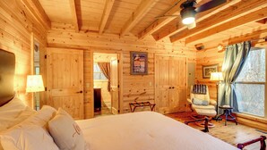 Un dormitorio de cabaña de madera con cama, una mecedora, un escritorio y una ventana con cortinas.