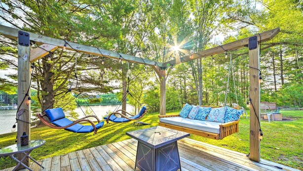 A wooden deck with a swing chair, a cushioned bench, and a glass-top table. - Riverfront Home w/ Dock ~ 6 Mi to Cheboygan! (Cheboygan)