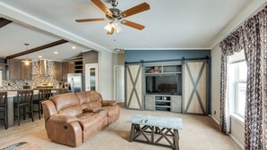 A spacious living room with a leather sofa, a coffee table, and a TV. There is a kitchen in the background with a stone backsplash and wooden cabinets. - Spacious Tierra Amarilla Ranch House w/ Deck! (Tierra Amarilla)