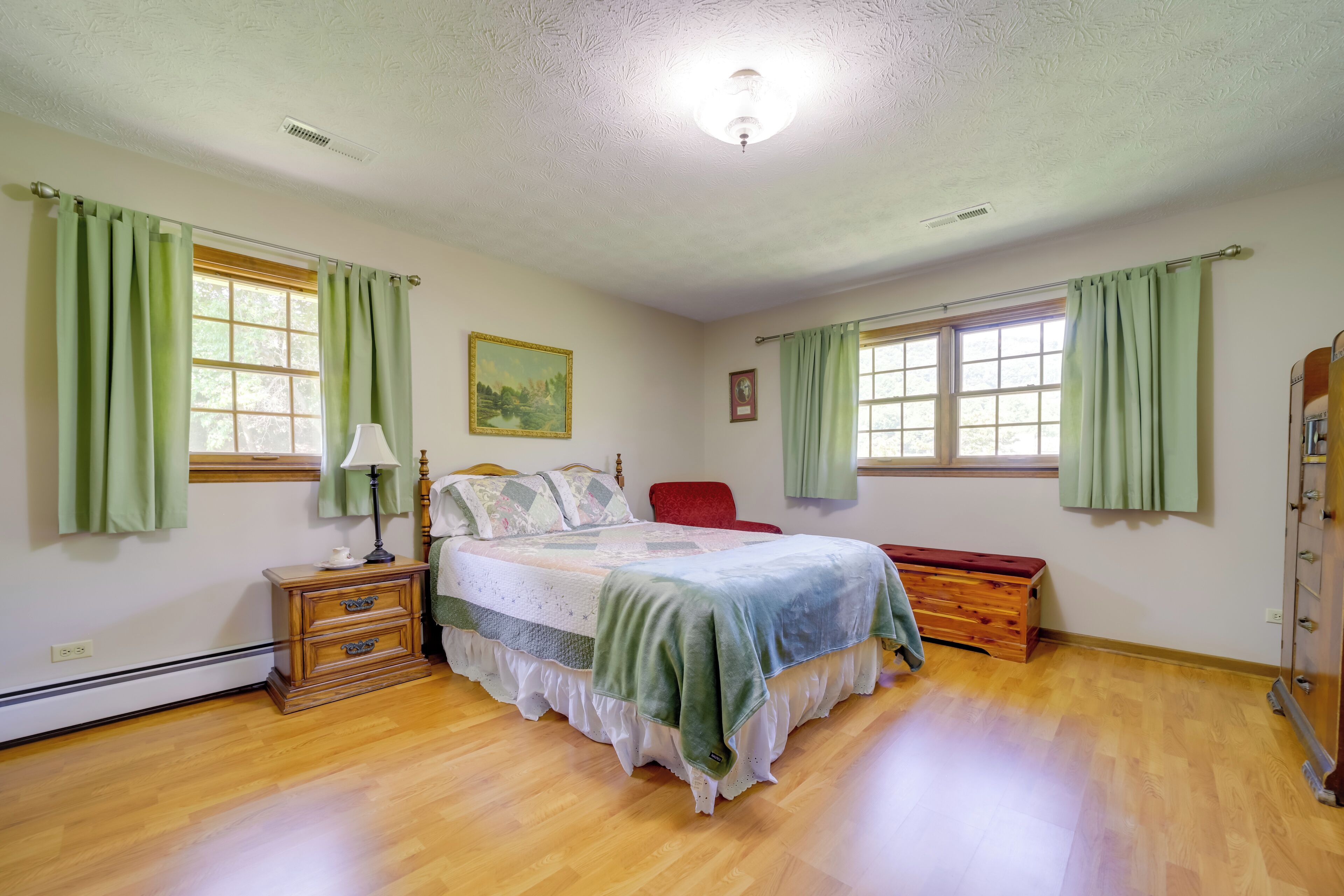 Une chambre à coucher avec un lit en bois, des rideaux verts, une table de chevet, une chaise rouge et une commode en bois.