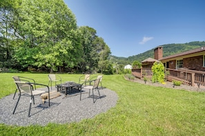 A patio with outdoor furniture, a brick building with a chimney, and a lush green landscape.