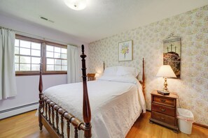 Ein Schlafzimmer mit einem hölzernen Himmelbett, einem Nachttisch mit Lampe, einem Wandspiegel und einem Fenster mit Vorhängen.