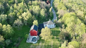 An aerial view of a property with two main buildings, a red barn, and a large white house with a driveway leading to a circular hot tub area.