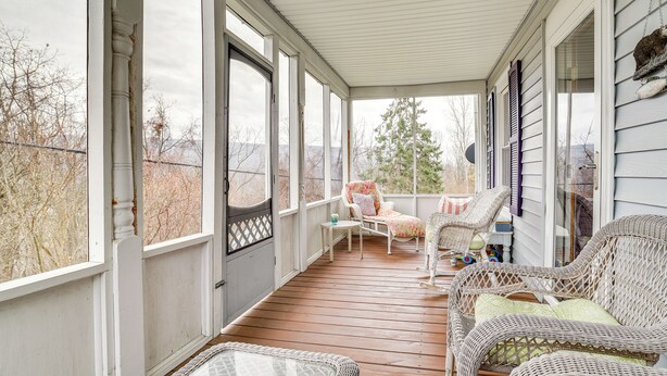 A covered porch with wicker furniture, large windows, and a view of trees and hills.