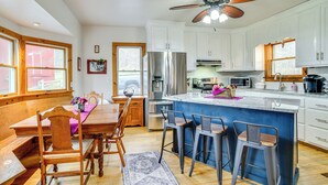 A modern kitchen with white cabinets, a large island with bar stools, wooden dining table, and a ceiling fan.