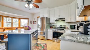 A modern kitchen with white cabinets, stainless steel appliances, a marble countertop, and a ceiling fan.