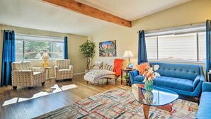 Een ruime woonkamer met een grote blauwe bank, gestreepten fauteuils, een houten salontafel en een kleurrijk vloerkleed.