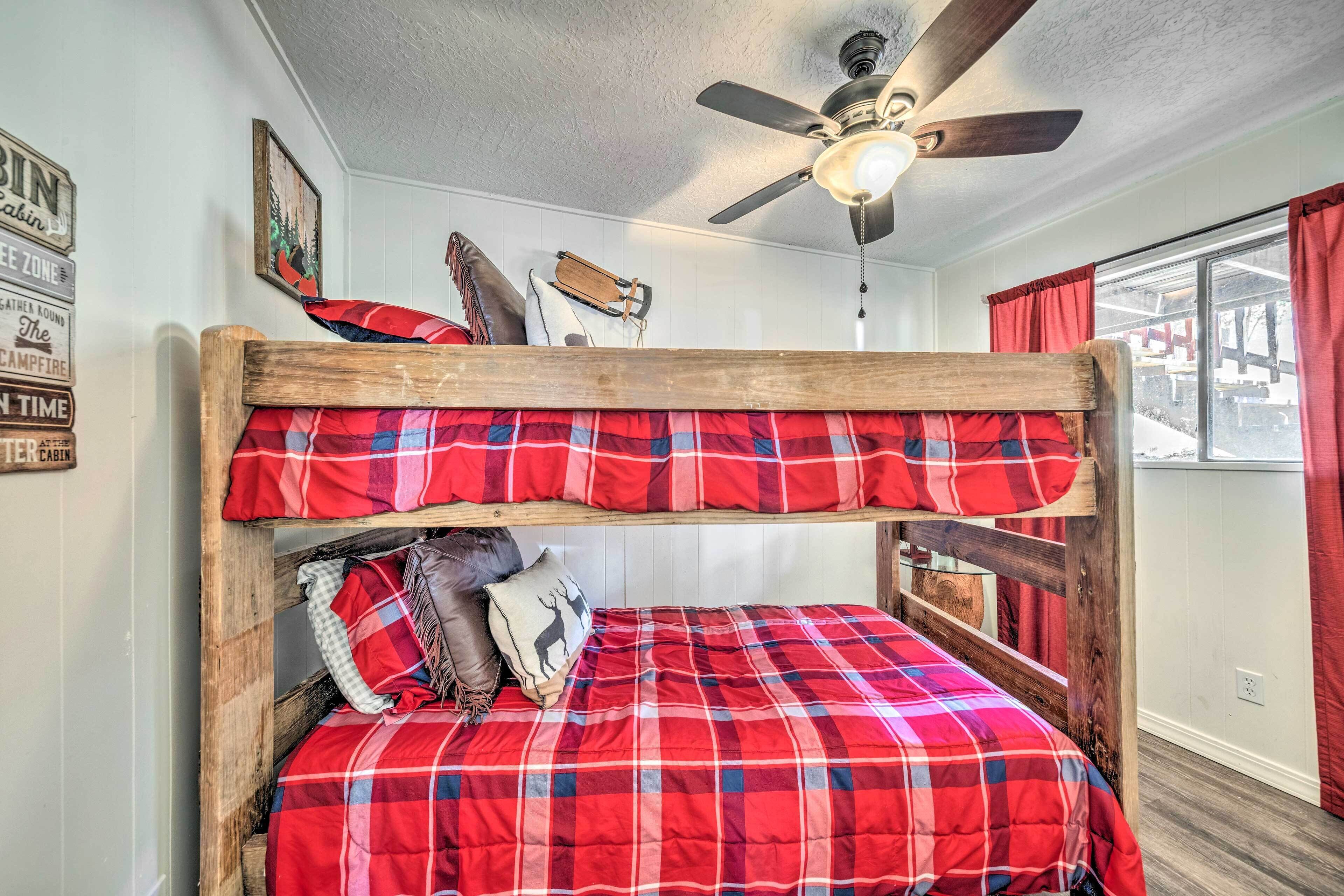 A bunk bed with red plaid bedding, a ceiling fan, and a window with red curtains.