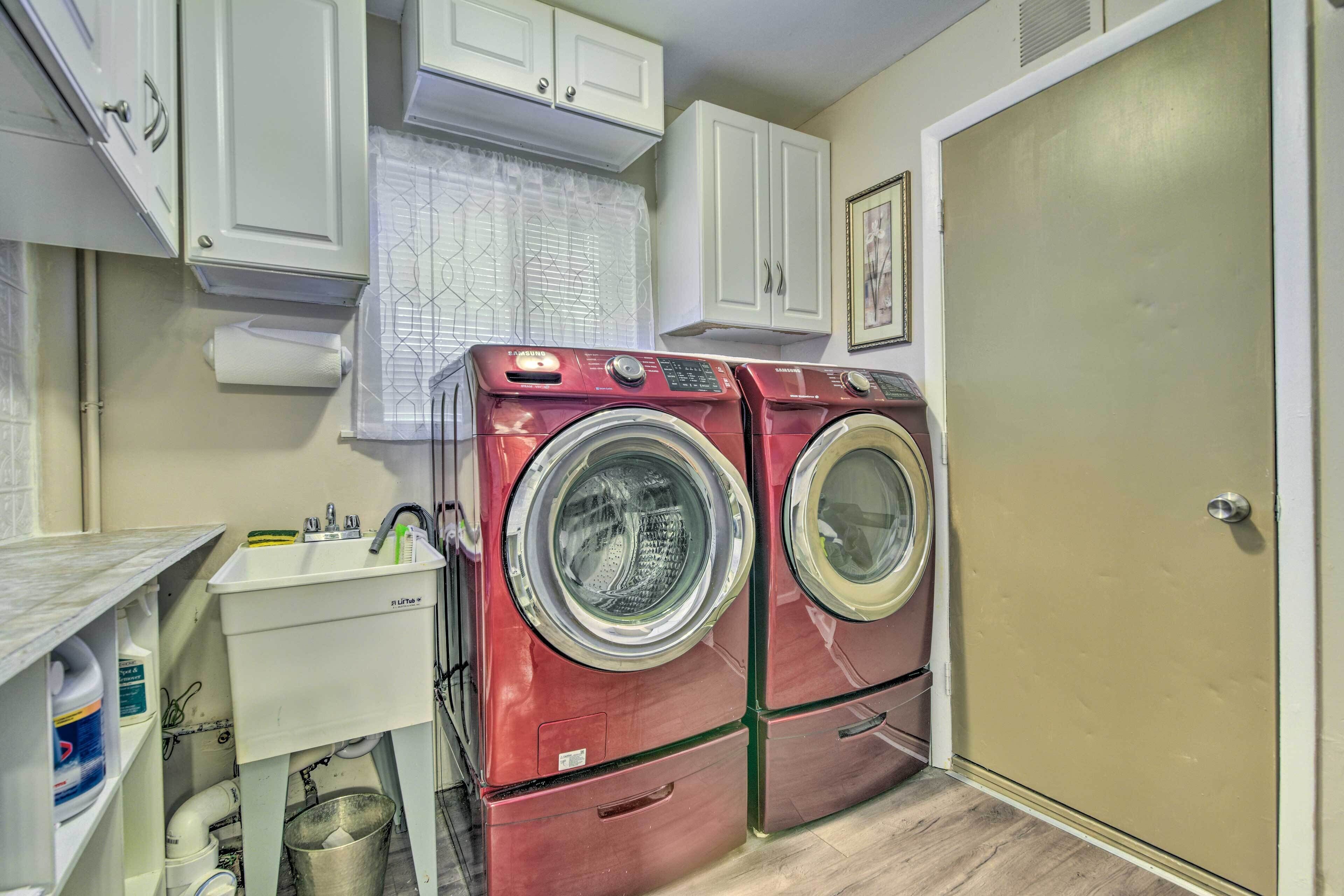 A laundry room with two red front-loading washers, a white sink, and cabinets.