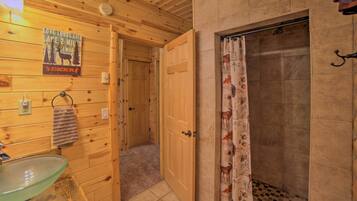 Bagno di una baita in legno con lavabo in vetro, tenda da doccia con stampe di animali e una porta che dà su un'altra stanza.