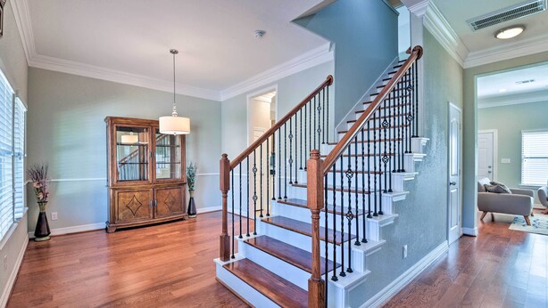 A spacious living room with hardwood flooring, a wooden staircase with a railing, and a built-in cabinet. - Spacious Houston Home ~ 16 Mi to NRG Stadium! (Houston)