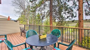 Eine Holzterrasse mit rundem Tisch und Stühlen, einem Vogelhäuschen und Blick auf Bäume und eine entfernte Landschaft.
