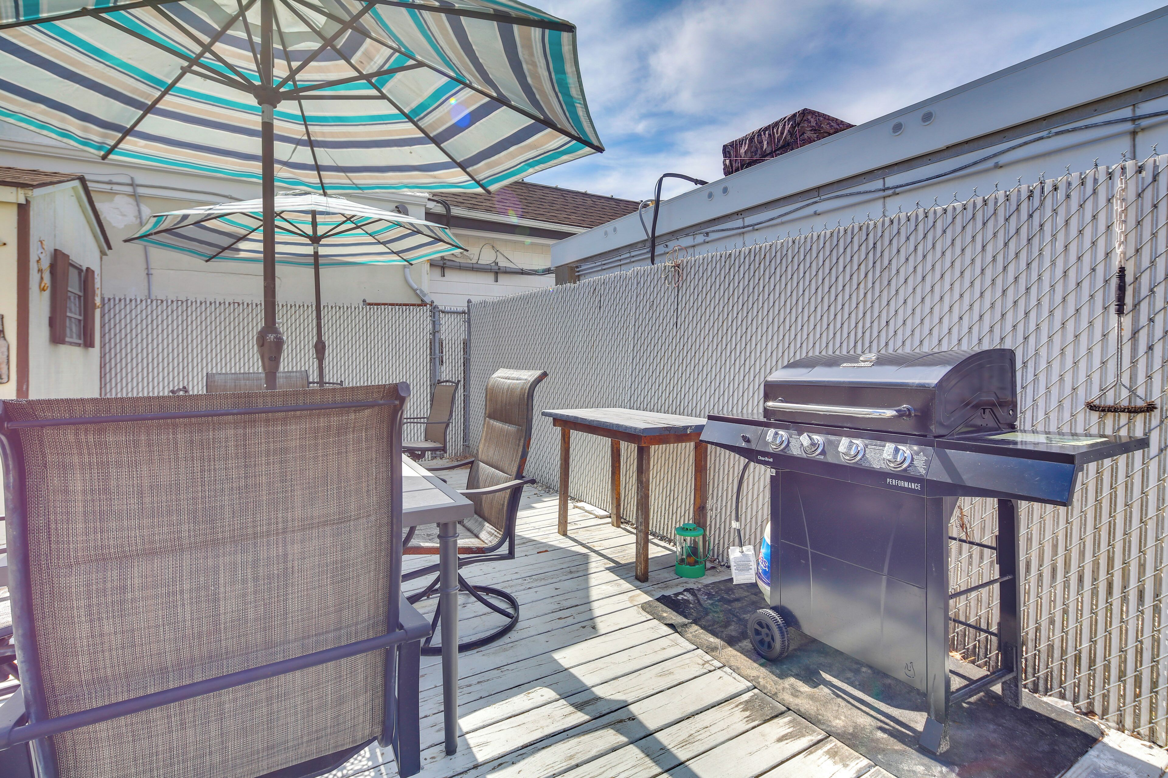 A backyard with a grill, chairs, a table, and a covered umbrella.