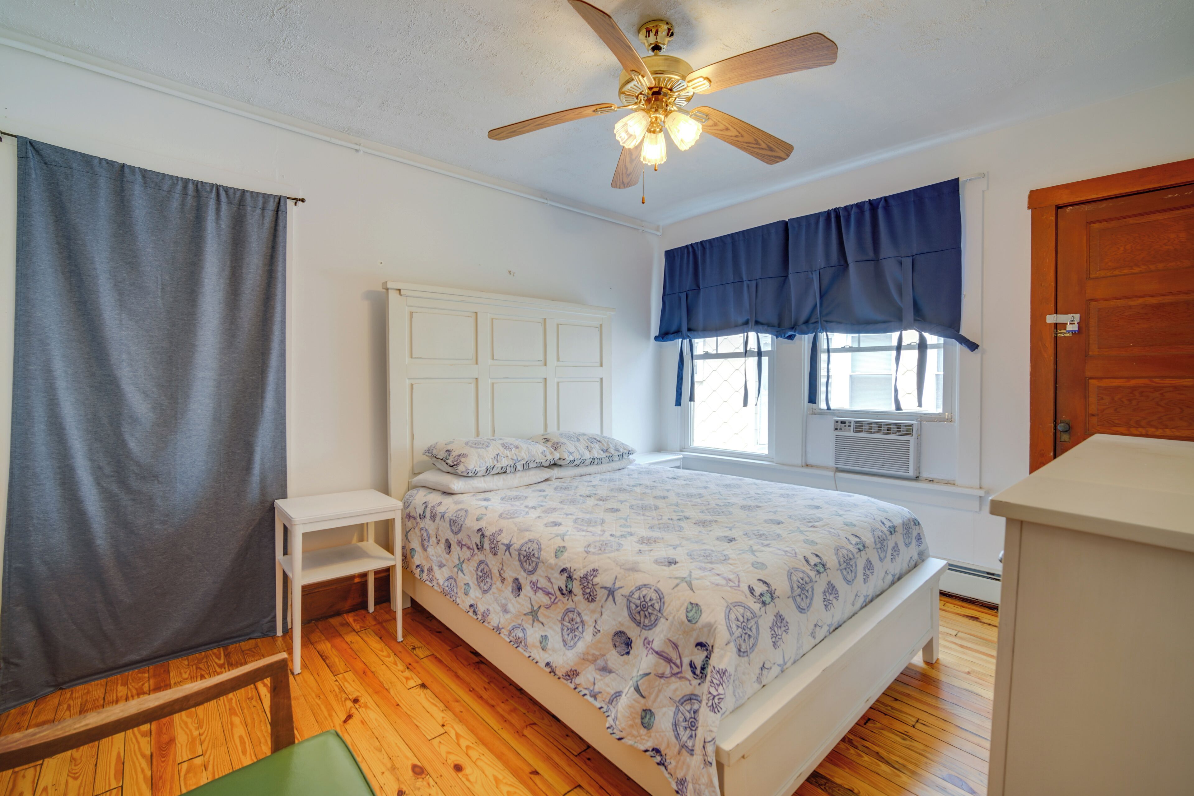 A bedroom with a bed, a ceiling fan, a window with curtains, and a wooden floor.