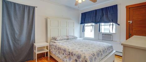 A bedroom with a bed, a ceiling fan, a window with curtains, and a wooden floor.