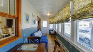 A room with a wooden table, blue sofa, and a window with floral curtains. - Wildwood Apartment - Porch & Enclosed Sunroom! (Wildwood)