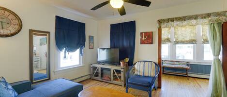 A living room with a sofa, armchair, wooden coffee table, television, and a ceiling fan.