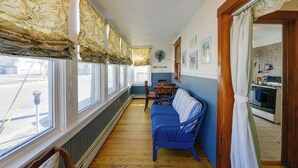 A narrow hallway with a blue sofa, wooden chairs, and a dining table. A kitchen with an oven and stove is visible through an open doorway. - Wildwood Apartment - Porch & Enclosed Sunroom! (Wildwood)