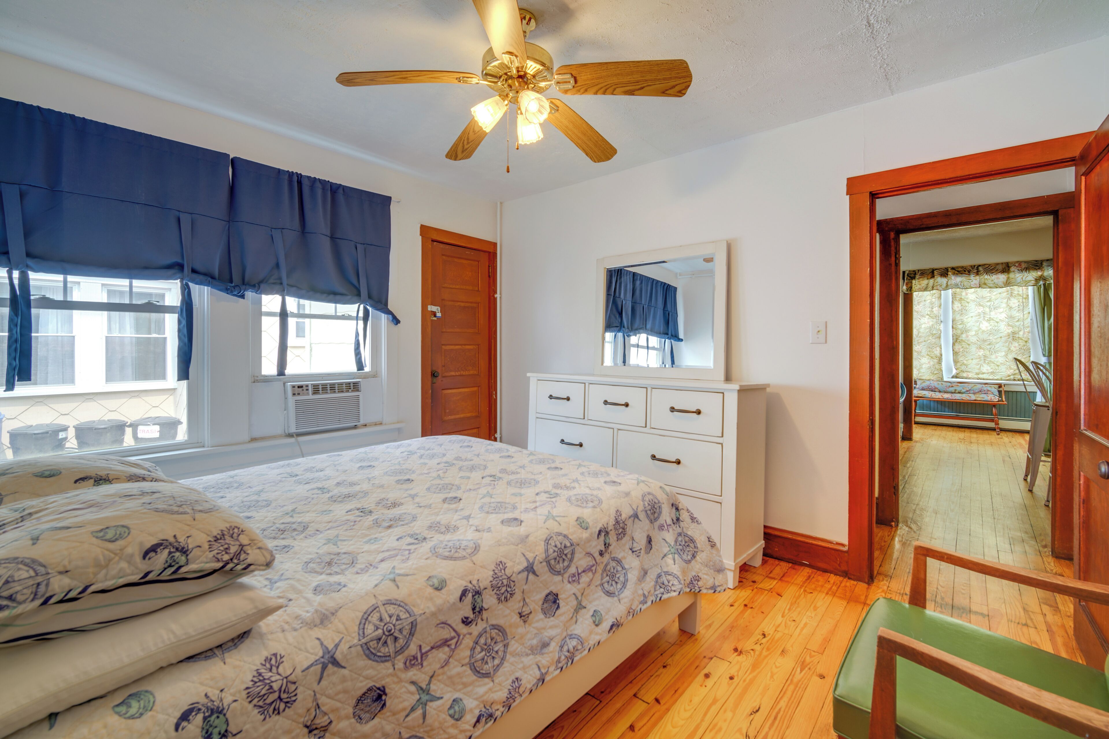 A bedroom with a bed, a dresser, a ceiling fan, and a view of the outside.