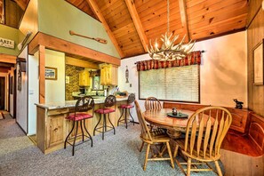 A cozy kitchen with wooden cabinets, a bar area, and a dining table with chairs. - Twain Harte Mountain Cabin w/ Deck - 3 Mi to Dtwn (Twain Harte)