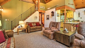 A spacious living area with a high ceiling, a staircase, a sofa, a recliner, and a wooden coffee table. - Twain Harte Mountain Cabin w/ Deck - 3 Mi to Dtwn (Twain Harte)