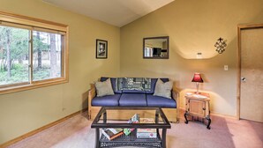 A living room with a sofa, a glass coffee table, a small cabinet, a lamp, a framed picture, and a window. - Trego Cabin w/ Mountain Views & Lake Access! (Trego)