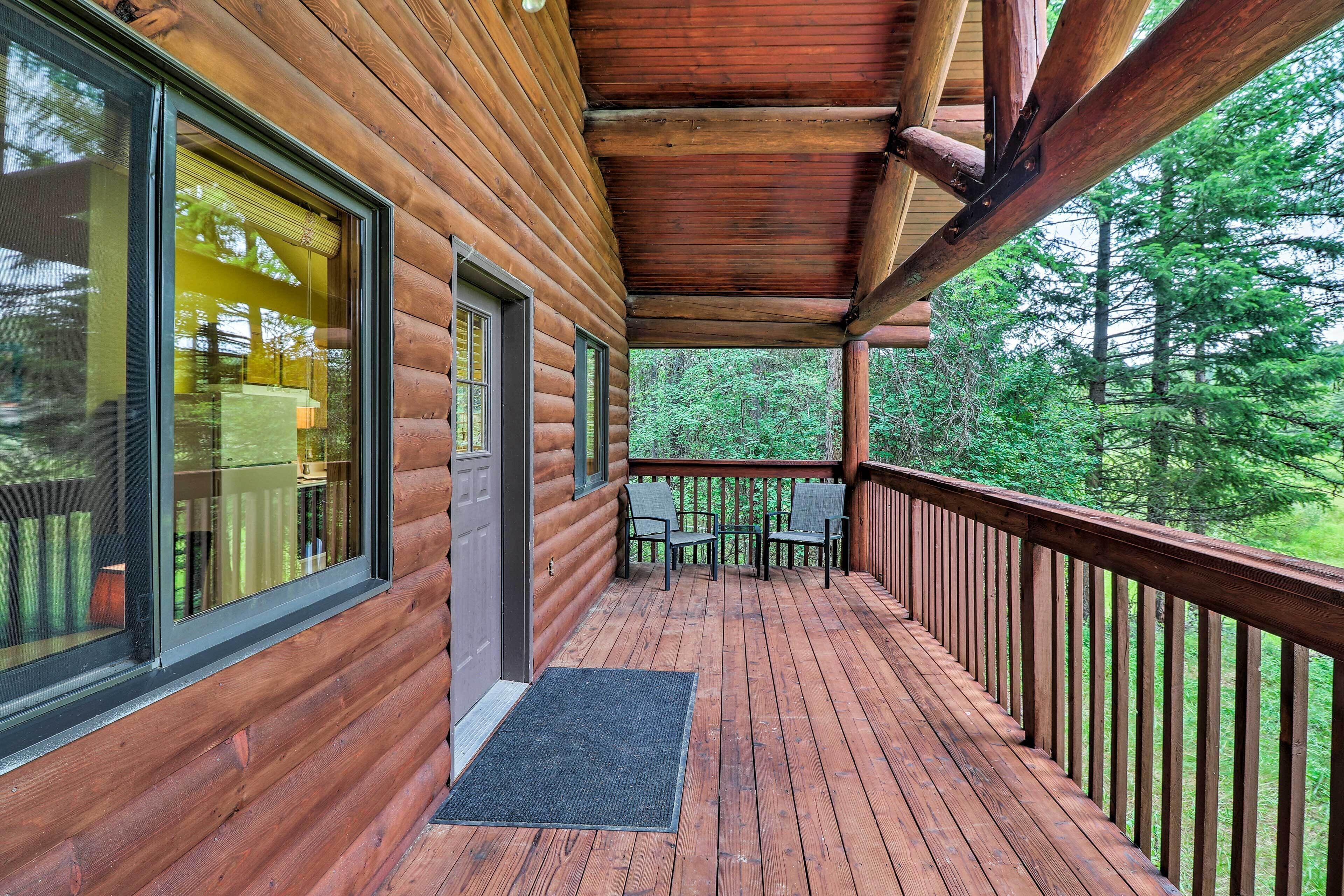 A wooden cabin with a covered porch, large windows, and a view of the forest.