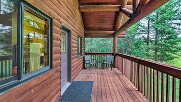 A wooden cabin with a covered porch, large windows, and a view of the forest.