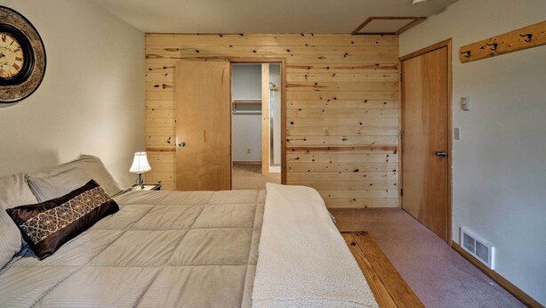 A bedroom with a bed, a nightstand, a lamp, and a wooden wall panel. - Trego Cabin w/ Mountain Views & Lake Access! (Trego)