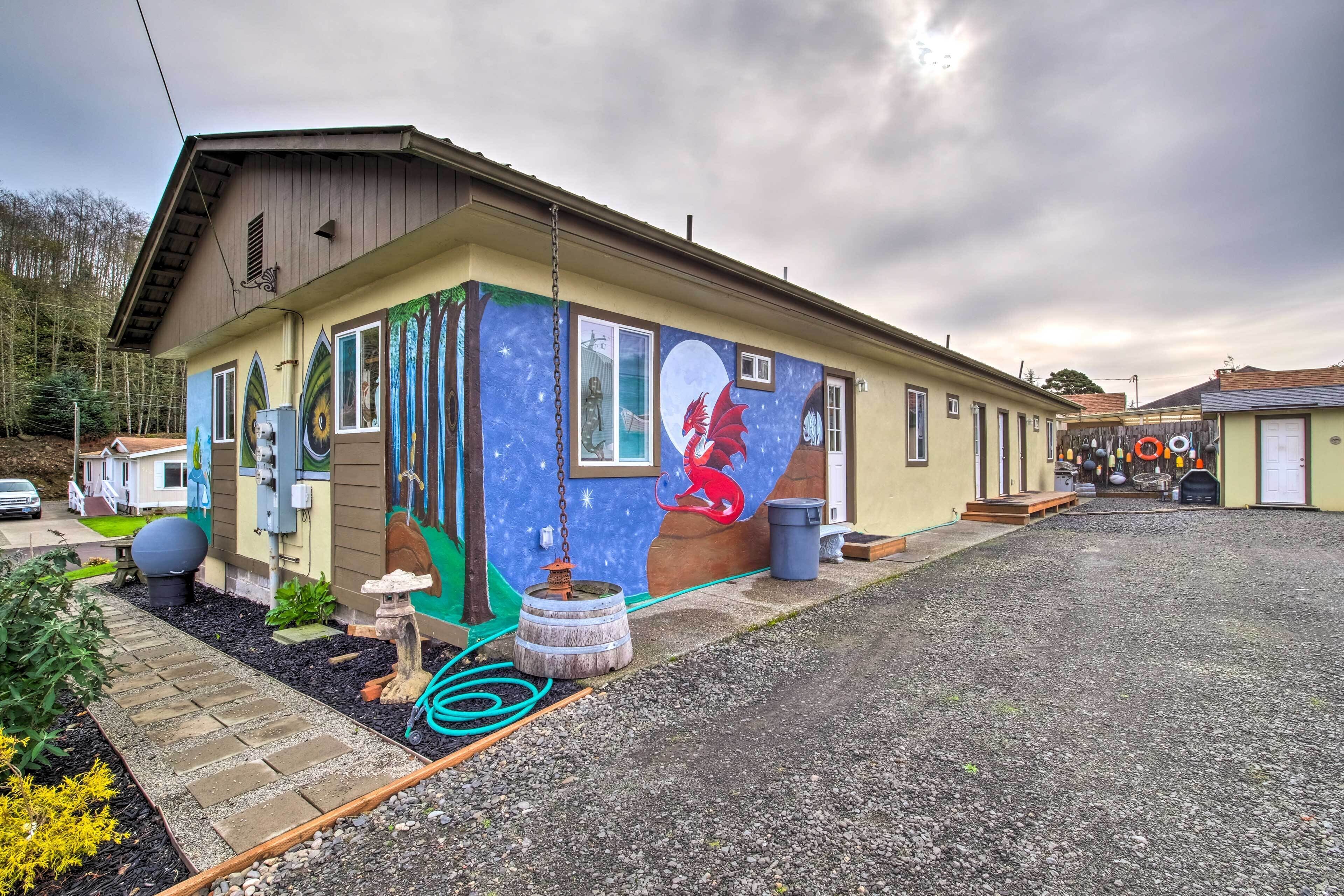 A house with a mural of a dragon on the side, a gravel driveway, and a small garden area.