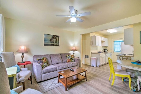 A living room with a sofa, chairs, a coffee table, a ceiling fan, and a kitchen area in the background. - Winchester Bay Apt Near Dunes & State Parks! (Reedsport)