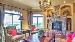 A spacious living room with a stone fireplace, large windows, and comfortable seating. - Spacious Grand Junction Home w/ Mountain View (Grand Junction)