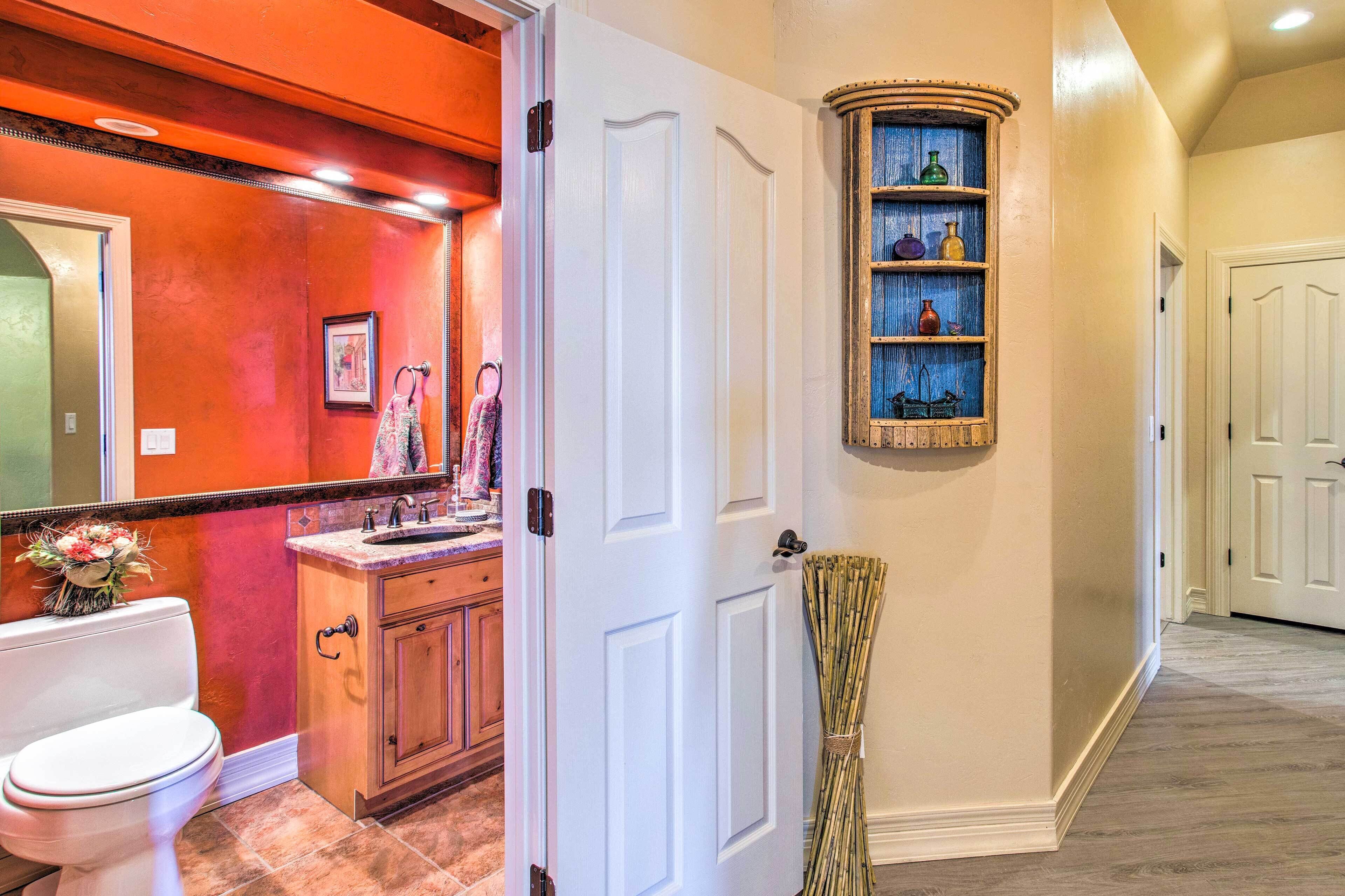 Une salle de bain comprenant des toilettes, un lavabo et un meuble de rangement, ainsi qu'un couloir avec une porte et une étagère où sont disposés des objets décoratifs.