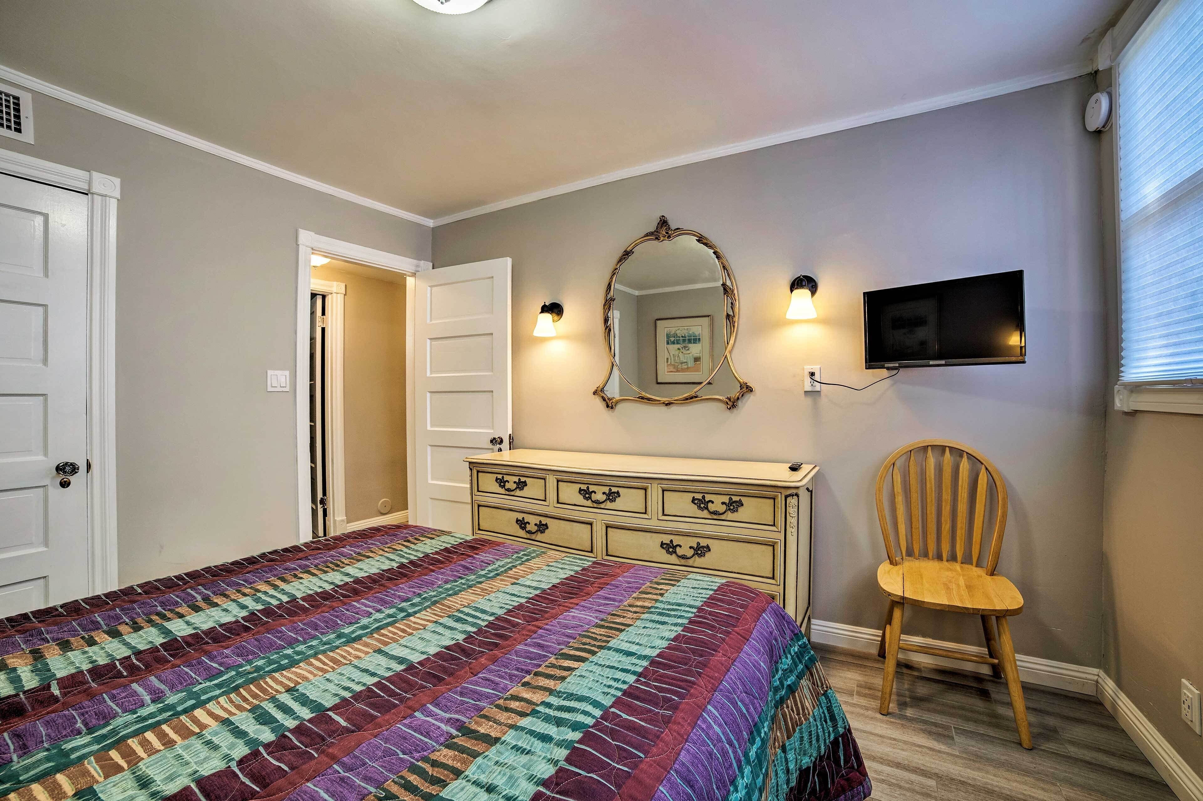 Un dormitorio con cama, cómoda, silla, televisor y puerta.