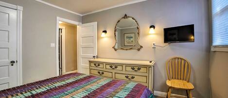 Un dormitorio con cama, cómoda, silla, televisor y puerta.