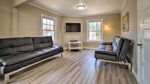 Een woonkamer met een zwarte leren bank, een relax fauteuil, een flatscreen televisie en een klein wit tafeltje.