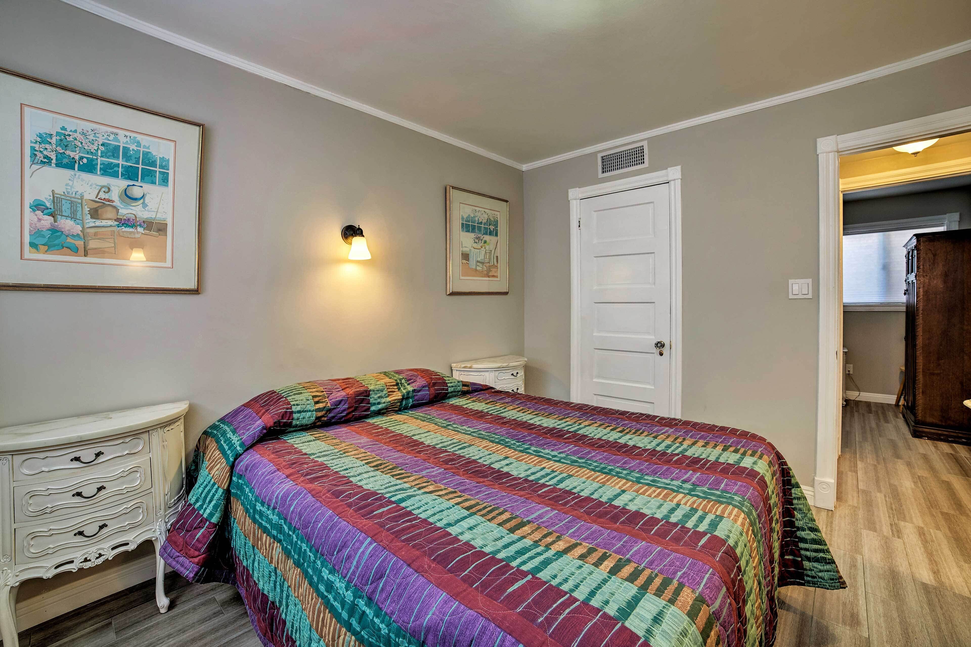 Um quarto com cama, mesa de cabeceira, penteadeira e duas fotografias emolduradas na parede.