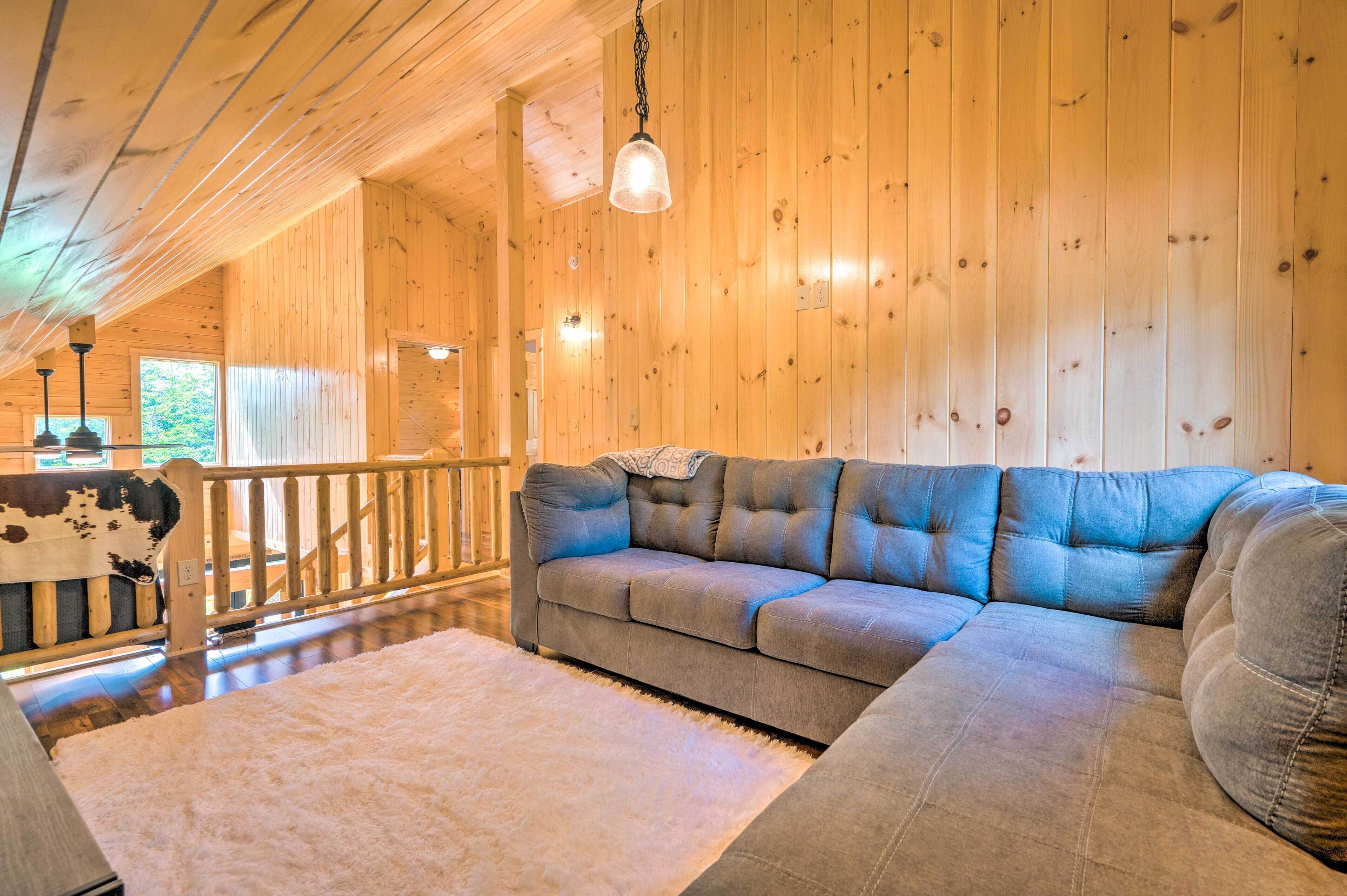 A cozy wooden interior with a sectional sofa, a fluffy rug, and a wooden railing.