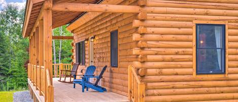 Une cabane en rondins avec une véranda, deux fauteuils à bascule et une petite fenêtre.
