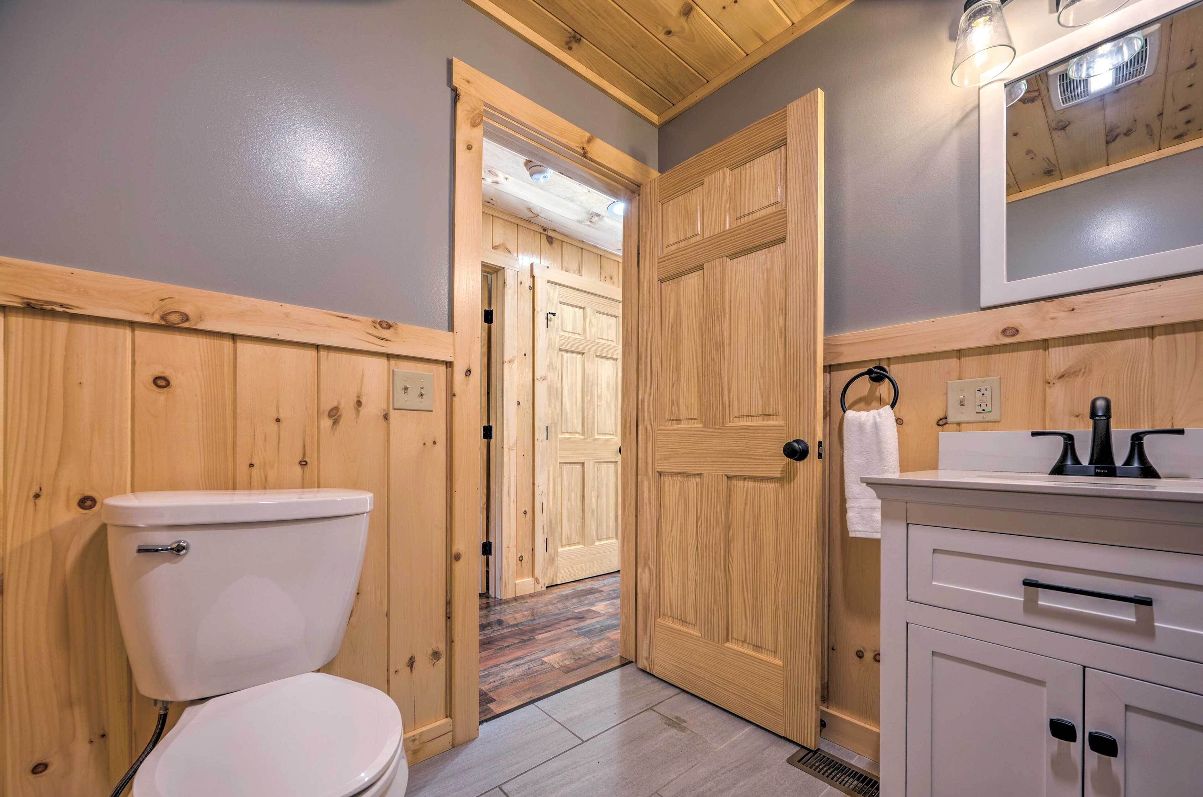 Een badkamer met een houten wastafelmeubel, een toilet en een deur naar een andere kamer.